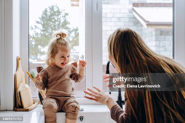 mom and little daughter play with water in the sink in the kitchen. a beautiful young woman and a 3 year old girl wash their faces at home. teaching hygiene procedures for children - child washing hands stock pictures, royalty-free photos & images