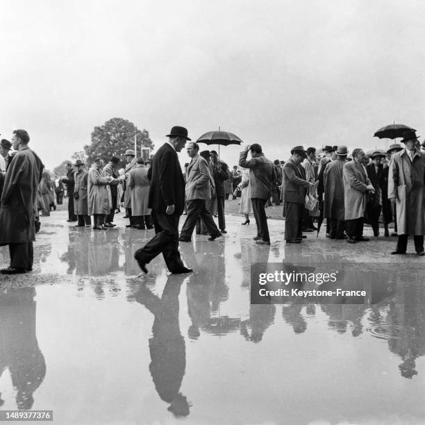 Spectateurs au milieu d'une flaque d'eau géante à l'hippodrome de Chantilly lors du prix du Jockey Club de Paris, le 13 juin 1954.