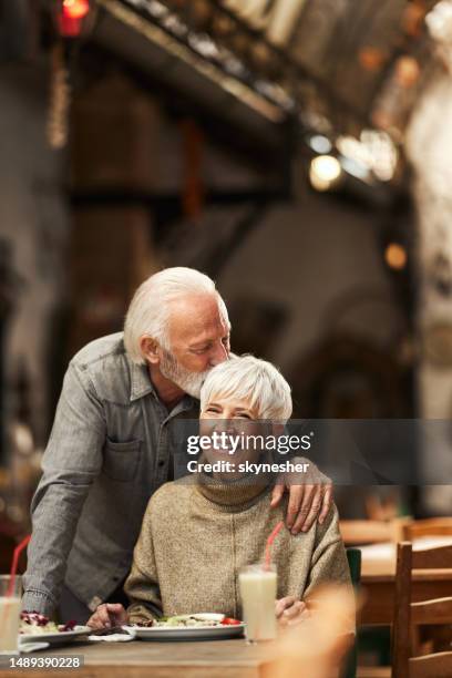 loving senior man kissing his wife in a restaurant. - old couple restaurant stock pictures, royalty-free photos & images