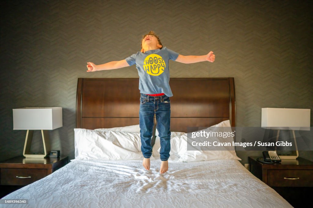 Joyful boy jumping high in the air on a hotel bed