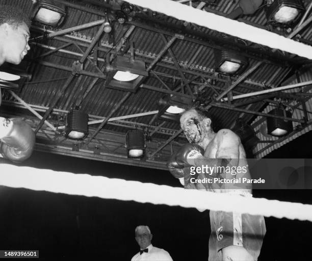 American heavyweight boxer Muhammad Ali, partially visible at the left, fight referee George Smith, and British heavyweight boxer Henry Cooper, blood...