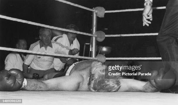 British heavyweight boxer Richard Dunn out for the count, as his opponent's manager Andy Smith celebrates in the background after his British,...