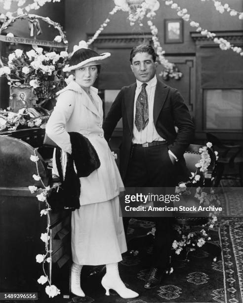 American boxer Johnny Dundee wearing a dark suit with a white shirt and tie, and his wife, Lucille, who wears a light suit and a dark hat with white...
