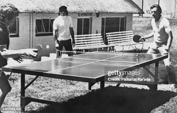 German-born racing driver Jochen Rindt playing British racing driver Graham Hill at table tennis, as British racing driver Jackie Stewart looks on,...