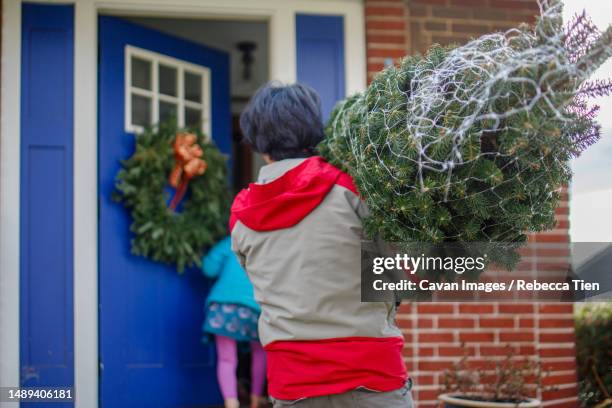 a man carries christmas tree into home with daughter in background - columbus ohio winter stock pictures, royalty-free photos & images