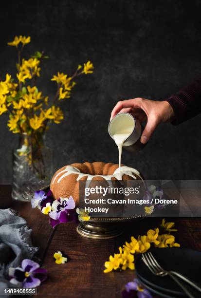 hand pouring icing on bundt cake decorated with flowers - forsythia stock pictures, royalty-free photos & images
