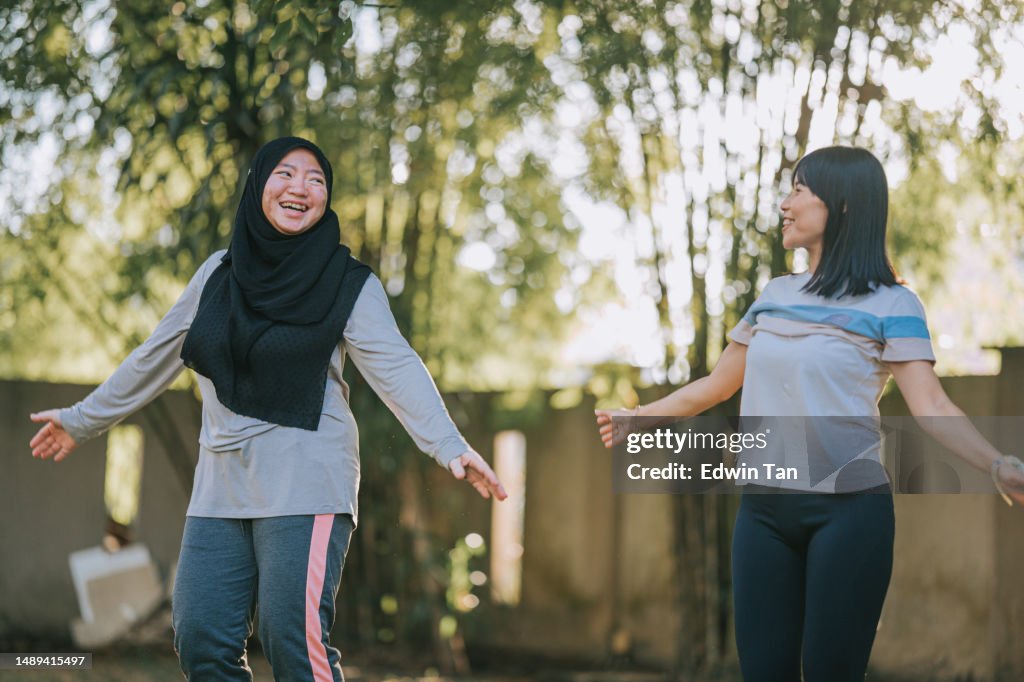 Asian Malay woman in hijab with vitiligo skin condition jumping jack warm up exercising with her female friend