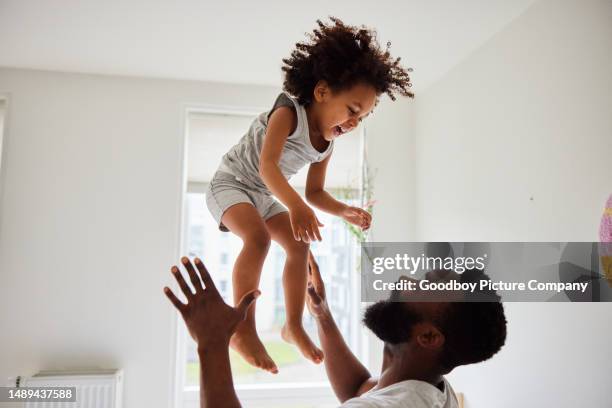 dad tossing his laughing son up in the air while playing at home - dad throwing kid in air stockfoto's en -beelden