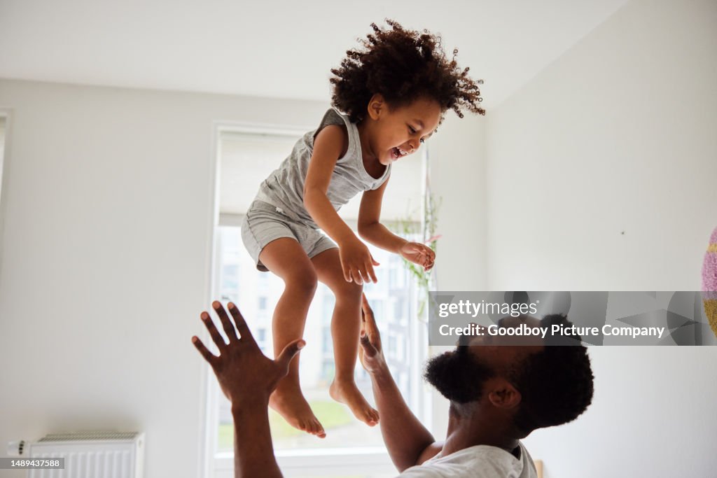 Dad tossing his laughing son up in the air while playing at home