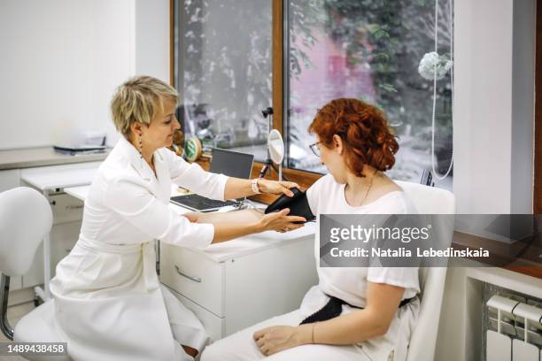 doctor's appointment: a woman in her middle age measures the blood pressure of a middle-aged woman patient in the examination room - misuratore foto e immagini stock