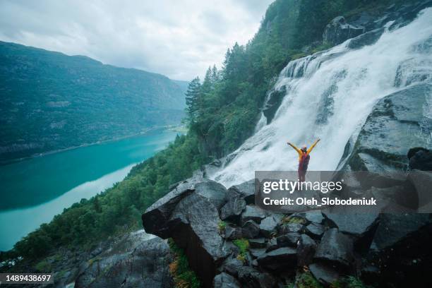 mujer levantando los brazos cerca de la cascada en las montañas de noruega - glaciar de briksdalsbreen fotografías e imágenes de stock