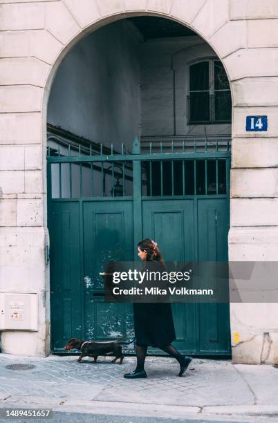 Woman with a dog is walking down the street on April 26, 2023 in Paris, France. Famous for its iconic landmarks, Paris is considered one of the most...