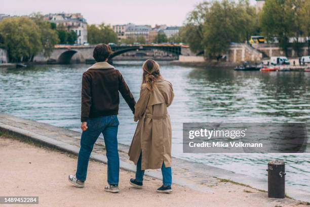 Young couple is walking along the Seine on April 26, 2023 in Paris, France. Famous for its iconic landmarks, Paris is considered one of the most...