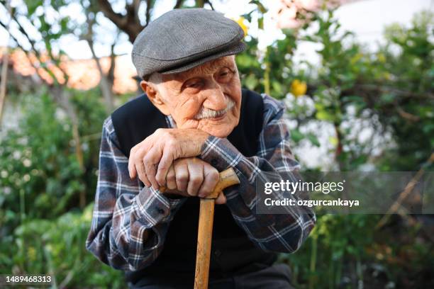 älterer mann sitzt auf einem stuhl - spazierstock stock-fotos und bilder