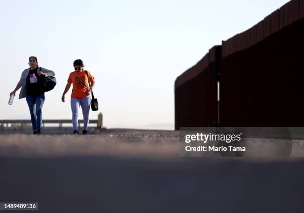 Immigrants who are seeking asylum in the United States walk along the border fence on their way to surrender to be processed by U.S. Border Patrol...