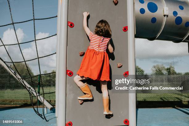 a little girl scales a climbing wall in a play park on a sunny day - six year old stock pictures, royalty-free photos & images