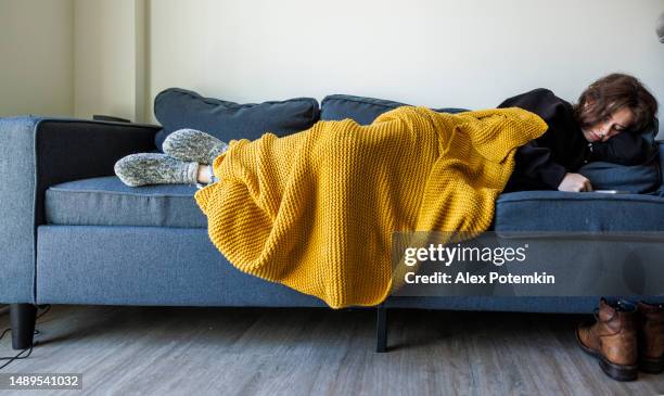 finding comfort at home: tired woman in yellow blanket rests on sofa with smartphone during sunny morning - woman sleeping stock pictures, royalty-free photos & images