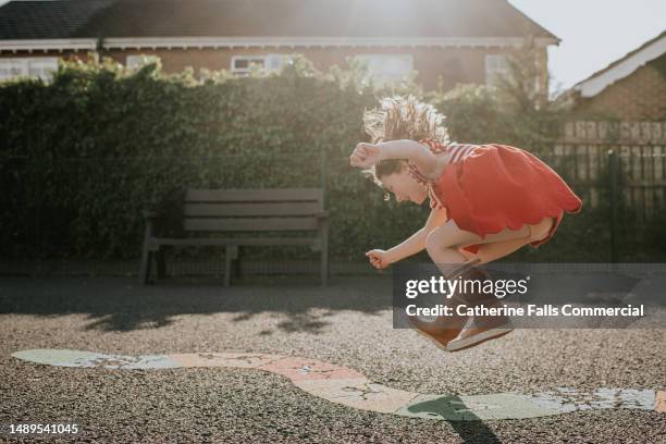 a little girl jumps on a colourful play park hopscotch snake - leap day stock-fotos und bilder