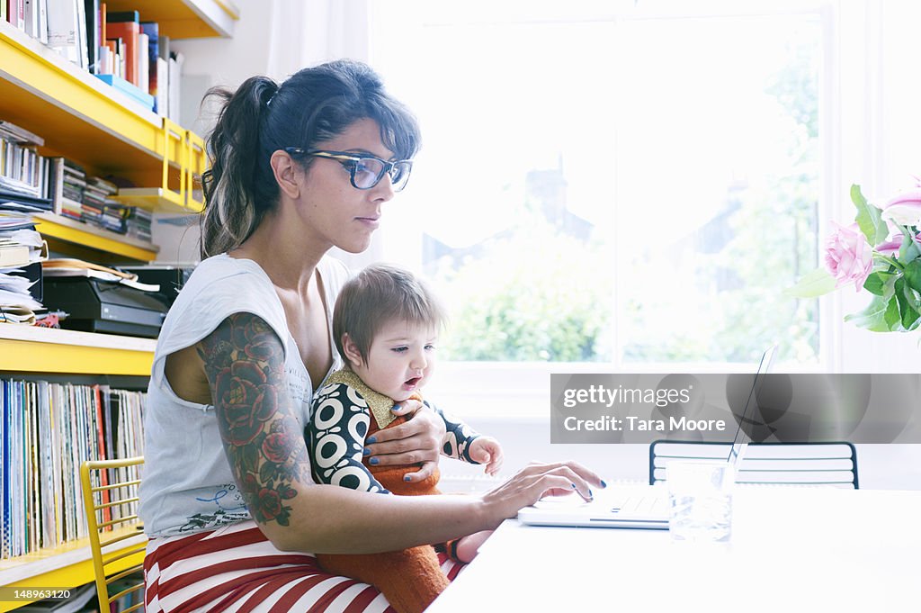 Mother with baby in lap working on laptop at home