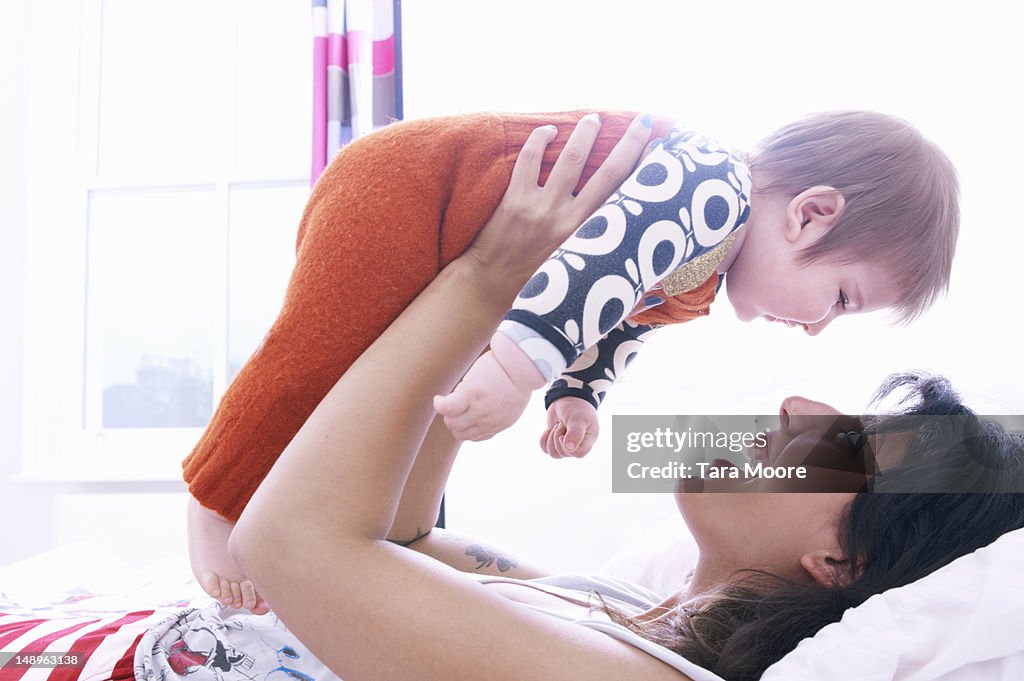 Mother holding baby face to face on bed