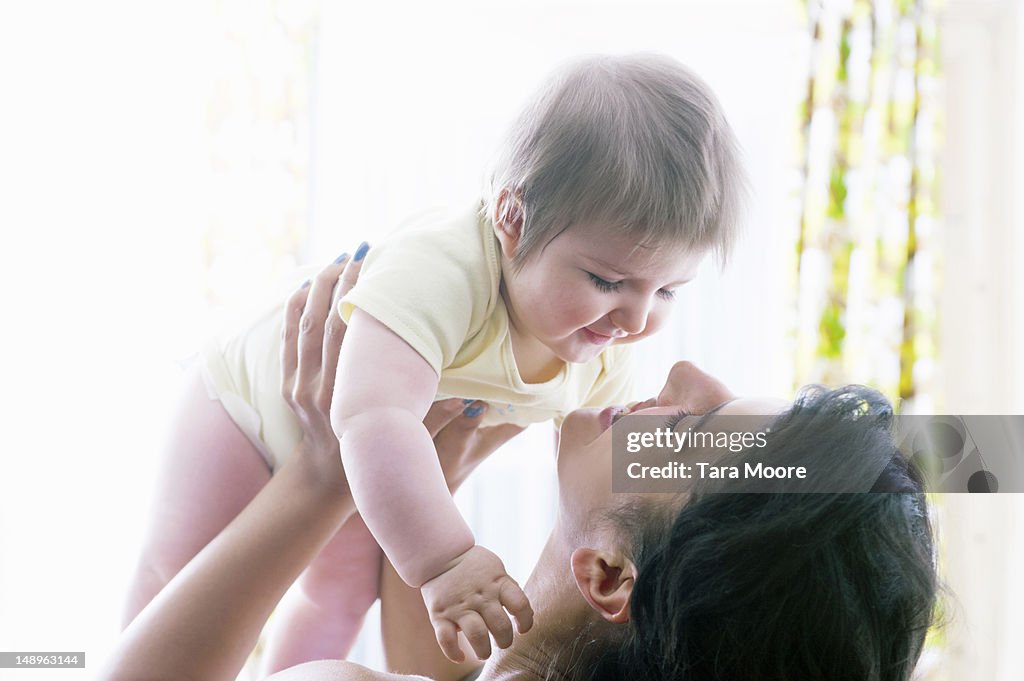 Mother smiling holding baby up in room