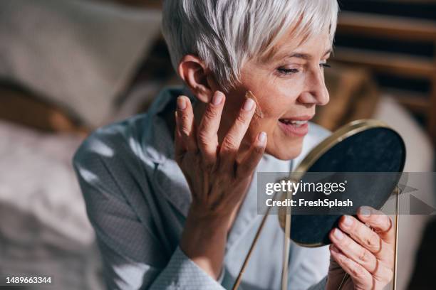 a happy beautiful woman in pajamas looking herself in the mirror while relaxing at home - human skin stock pictures, royalty-free photos & images