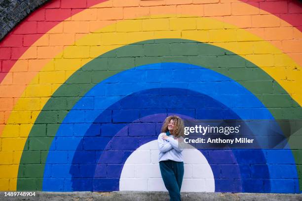 curly hair woman in front in front of rainbow painted on wall - colorful mural stock pictures, royalty-free photos & images