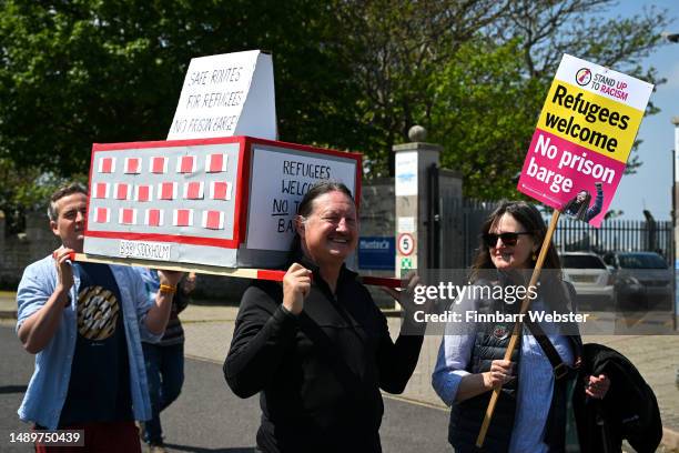 Protesters hold a model of the Bibby Stockholm barge as they march to the port during a rally against the UK government's plans to house 500 migrants...