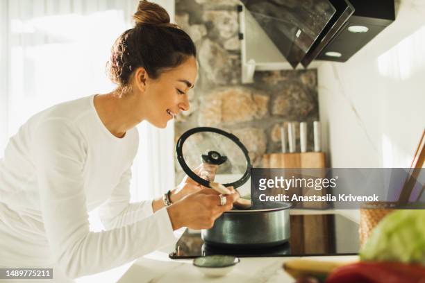 woman making lunch in the kitchen and stirring soup. - cookery stock pictures, royalty-free photos & images