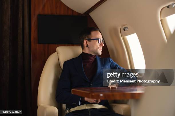 elegant businessman a blazer in eyeglasses private airplane jet, looking through windows - rich people stock pictures, royalty-free photos & images