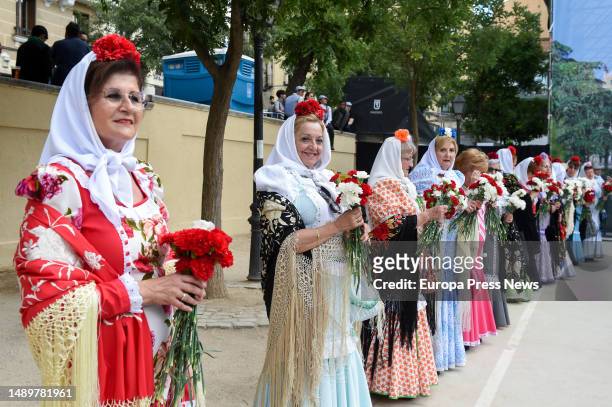 Women dressed as chulapas hand out red and white carnations at Las Vistillas on May 13, 2023 in Madrid, Spain. The San Isidro festivities are held in...