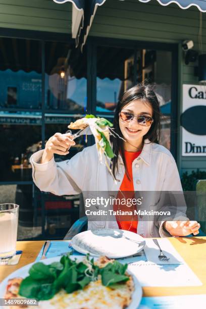 young asian woman holds a piece of pizza in outdoor summer cafe. - pizzeria ストックフォトと画像