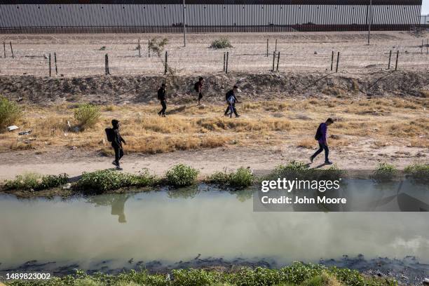 Honduran migrants walk along the U.S. Side of the Rio Grande and past an emptied-out migrant camp after crossing over from Mexico on May 13, 2023 to...