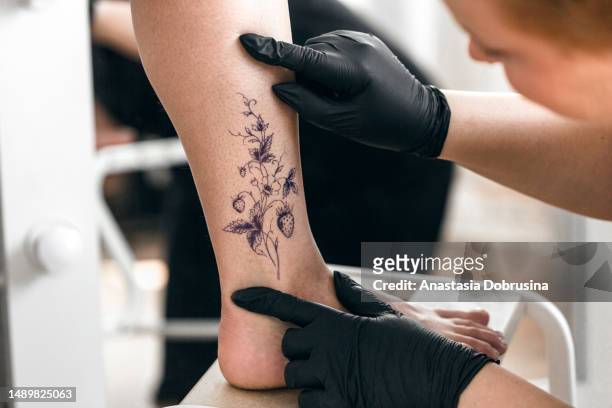 tattoo artist removing the tracing paper from a leg in a tattoo studio - black glove stock pictures, royalty-free photos & images