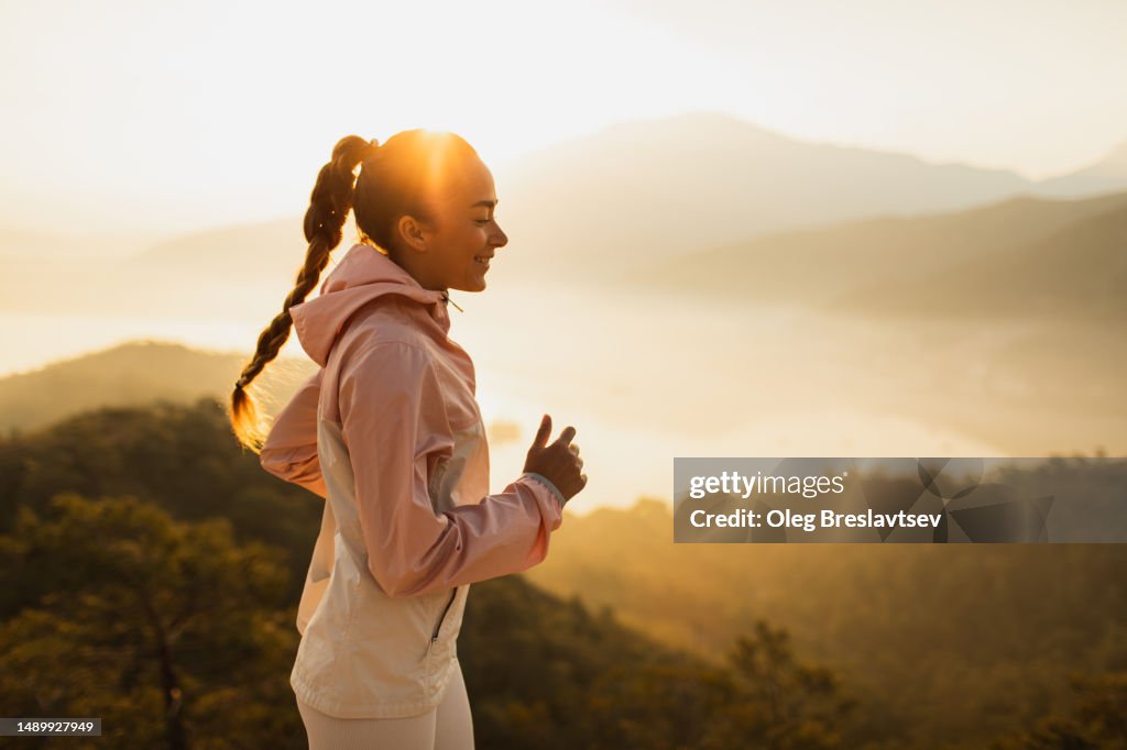 Happy young woman running outdoors with mountain view at sunset
