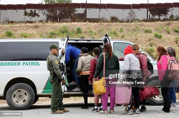 Border Patrol agent keeps watch as immigrants enter a vehicle to be transported from a makeshift camp between border walls, between the U.S. And...