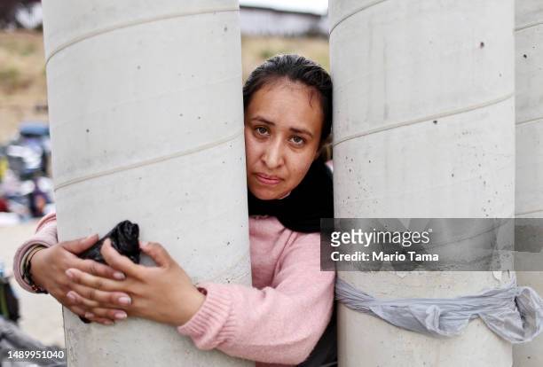 Colombian immigrant stands for a photo while grasping part of the border barrier at a makeshift camp between border walls, between the U.S. And...