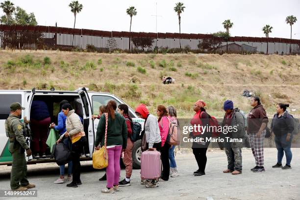 Border Patrol agent keeps watch as immigrants enter a vehicle to be transported from a makeshift camp between border walls, between the U.S. And...