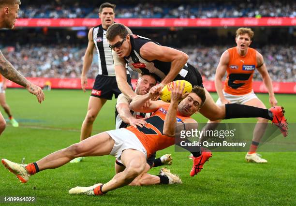Stephen Coniglio of the Giants handballs whilst being tackled by Tom Mitchell and Mason Cox of the Magpies during the round nine AFL match between...