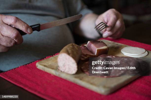 senior man sitting at table and eating sausage - sliced liverwurst stock pictures, royalty-free photos & images