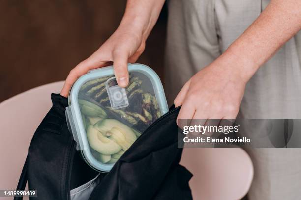 woman take a lunch box of healthy homemade food, zucchini pancakes and avocado salad in her backpack, healthy lunch to go for school and college students - jause stock-fotos und bilder