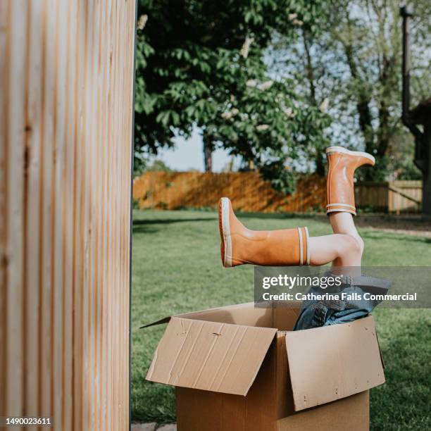 a child plays in a large cardboard box in a domestic garden. her feet hang out of the top of the box - lustige füße stock-fotos und bilder