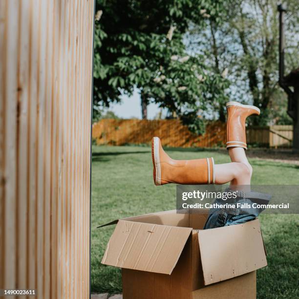 a child plays in a large cardboard box in a domestic garden. her feet hang out of the top of the box - girls open legs fotografías e imágenes de stock