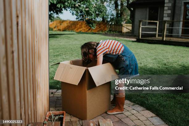 a little girl reaches into a large cardboard box - removing shoes stock pictures, royalty-free photos & images