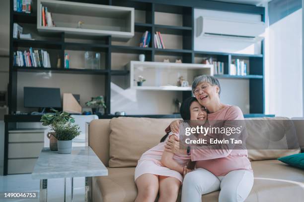 happy chinese grandmother hugging her granddaughter in living room - air conditioner family stock pictures, royalty-free photos & images