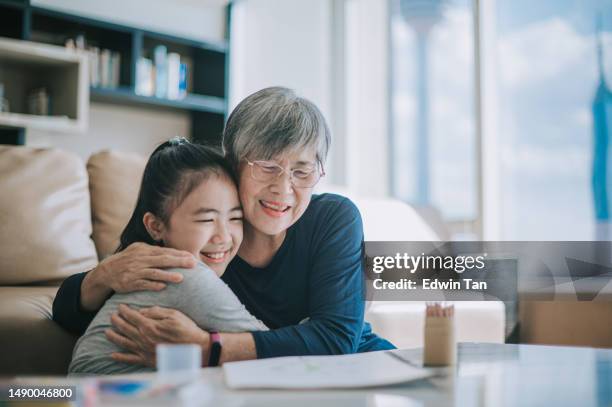 happy chinese grandmother hugging her granddaughter in living room - grandmas living room stockfoto's en -beelden