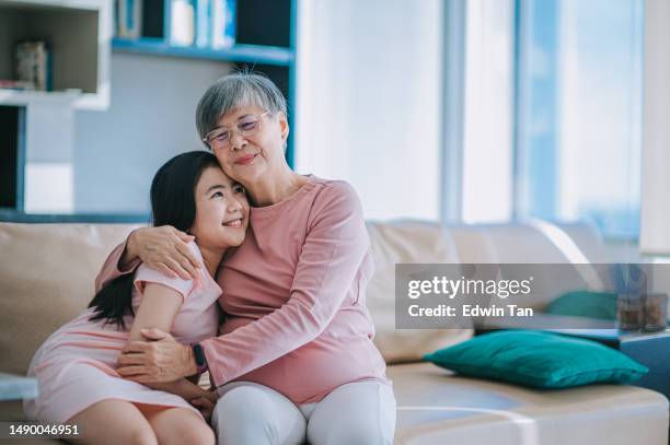 happy chinese grandmother hugging her granddaughter in living room - family wellbeing stock pictures, royalty-free photos & images