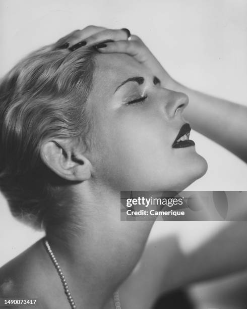 Young woman head tilted back, as if looking skyward with their eyes closed and her hand on her head.