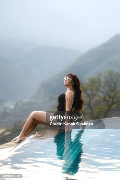 fashionable woman in black swimsuit sitting on pool with landscape of mountain background at sunset - pretty vietnamese women 個照片及圖片檔