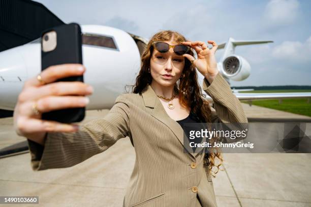 businesswoman posing for selfie in front of corporate jet - ijdel stockfoto's en -beelden